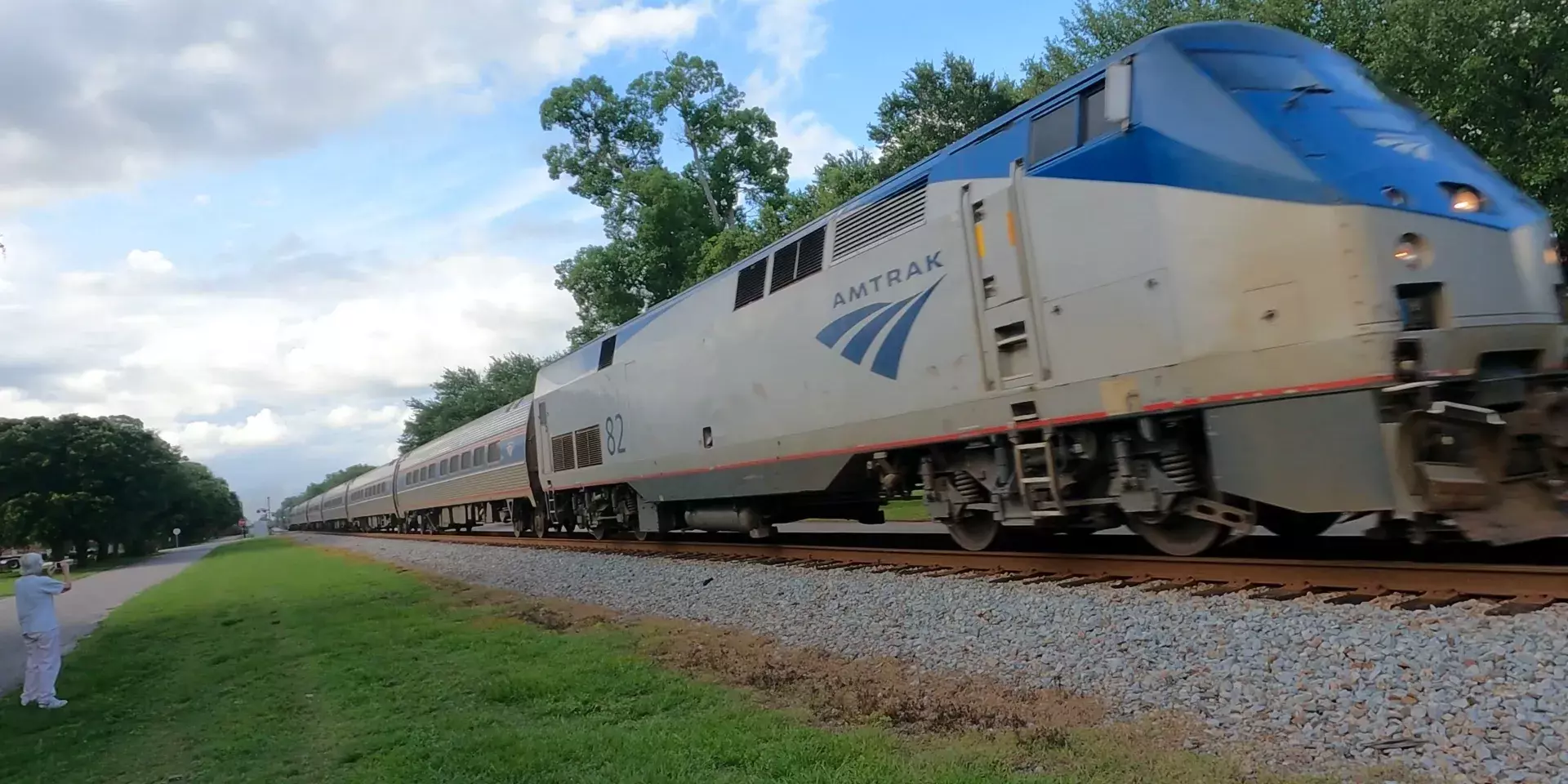 Amtrak passenger train passing on track with locomotive 82 and railfan photographing