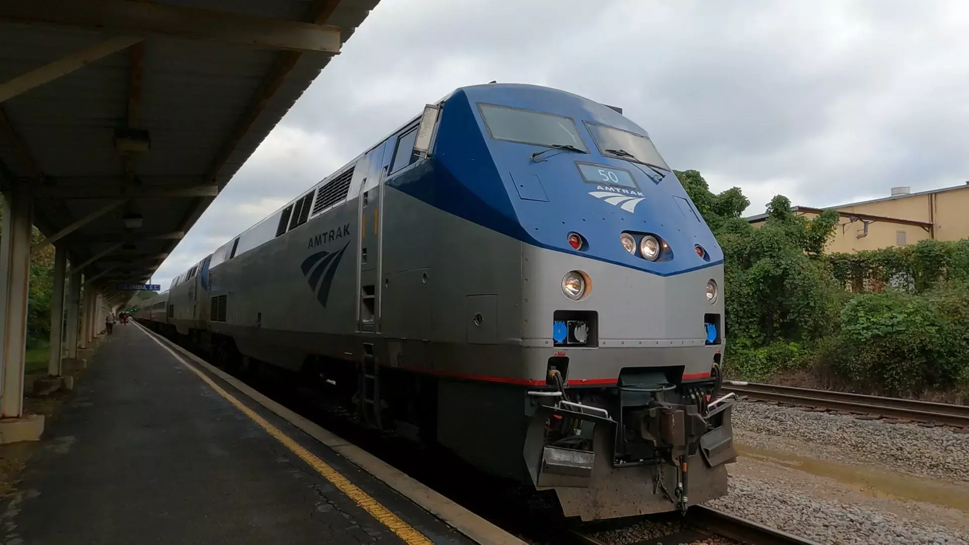 Amtrak locomotive 50 at station platform under cloudy sky with passenger cars behind