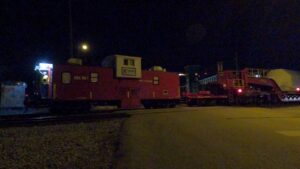 Red rail maintenance train at night with lit doorway and worker visible inside